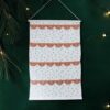 Advent calendar fabric hanging with orange numbered flaps over a white polka-dot background on a green wall.