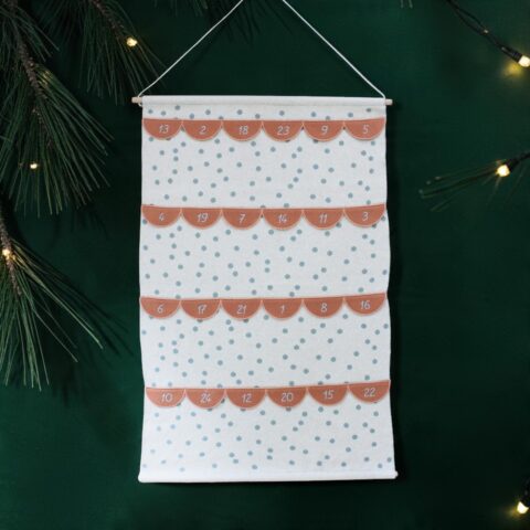 Advent calendar fabric hanging with orange numbered flaps over a white polka-dot background on a green wall.