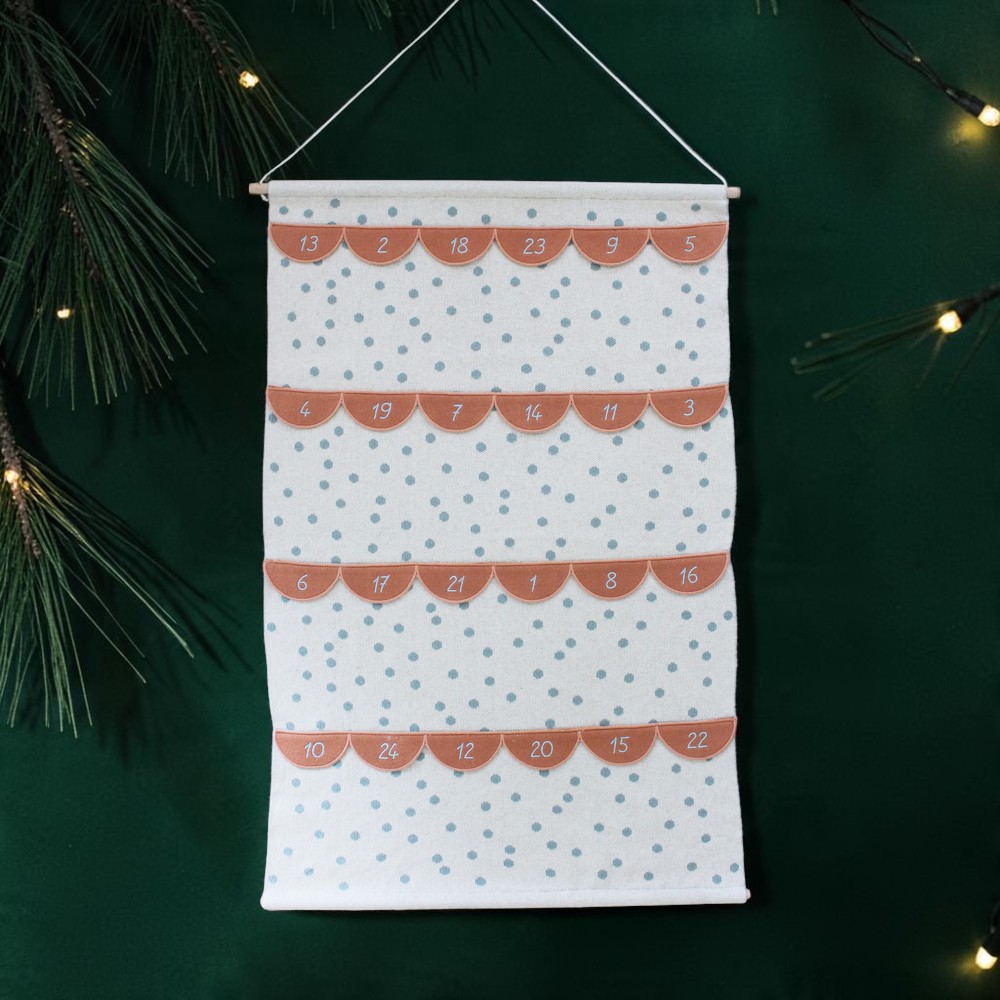 Advent calendar fabric hanging with orange numbered flaps over a white polka-dot background on a green wall.