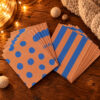 Greeting cards with blue polka dots and stripes fanned out on a warm wooden table, with fairy lights in the background.