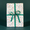 Gift box wrapped in white confetti-pattern paper with a teal ribbon and bow on a dark green background.