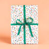 Gift box wrapped in terrazzo-speckled paper with a teal ribbon and bow on a peach background.