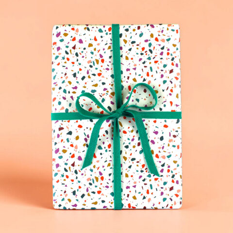 Gift box wrapped in terrazzo-speckled paper with a teal ribbon and bow on a peach background.