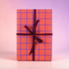 Gift box wrapped in orange paper with a purple plaid grid and a dark purple ribbon tied in a bow