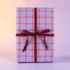 Lavender gift box with orange plaid pattern and a burgundy ribbon tied in a bow.