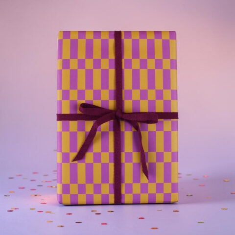 Gift box wrapped in yellow-and-purple checker paper with a purple ribbon, on a pastel background with confetti.