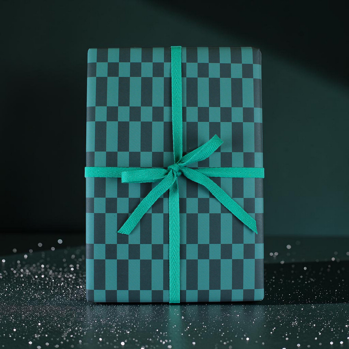 teal and dark-teal checkered gift box wrapped with a teal ribbon bow on a dark surface
