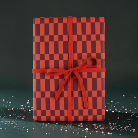 Gift box wrapped in red and burgundy checker paper with a red ribbon bow, on a dark green backdrop.