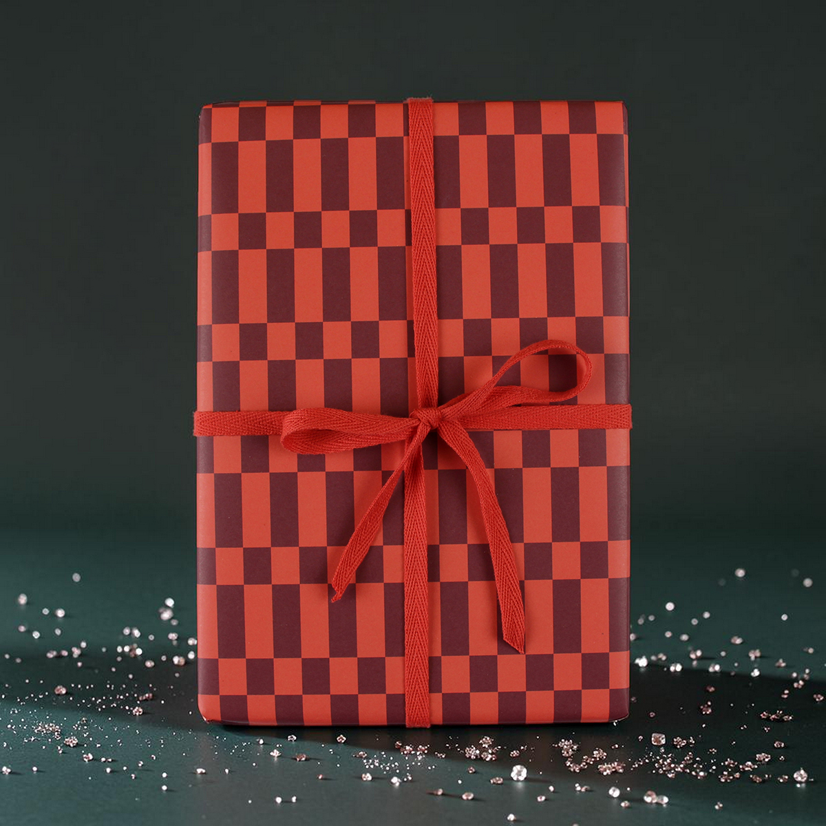 Gift box wrapped in red and burgundy checker paper with a red ribbon bow, on a dark green backdrop.