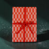 Gift box wrapped in red-and-pink checker-pattern paper with a red ribbon bow on a dark background for gifting.