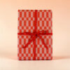 Gift box wrapped in red-and-pink checker paper tied with a red ribbon bow.