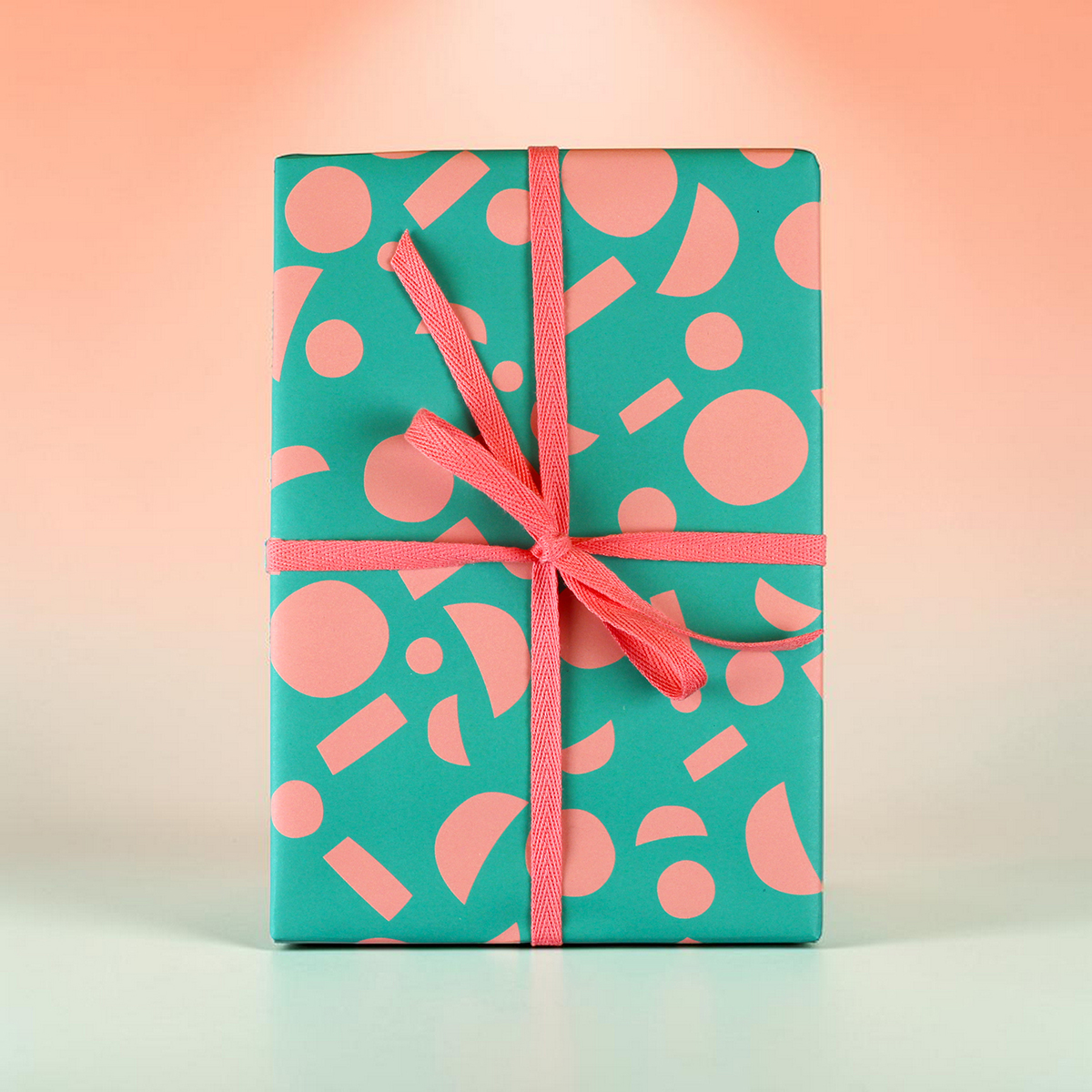 Teal gift box with pink geometric shapes and a pink ribbon bow on a pale gradient background.
