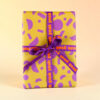 Yellow gift box with purple geometric wrap and a purple ribbon that reads 'yeah yeah yeah' in orange letters on the ribbon.