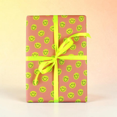 Gift box wrapped in pink paper with a repeating yellow smiley-face pattern and a bright yellow ribbon tied in a bow on top.