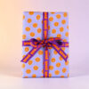 Gift box wrapped in lavender paper with orange smiley faces and a purple ribbon tied in a bow, saying 'yeah year' along the ribbon.
