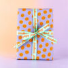 Gift box wrapped in lavender paper with orange smiley faces, tied with a turquoise ribbon bow that reads 'Schulkind'.