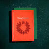 Red Christmas card with a wreath illustration and 'Merry Christmas' on the front, placed on a green envelope against a snow-speckled dark background.