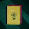 Yellow Christmas card with a leafy botanical illustration and 'Merry Christmas' text on a teal surface with a magenta backing.