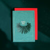 Teal Christmas card with gold text 'Frohes Fest' and a pine bow design on a red backing set against a dark green background.
