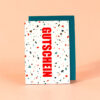 2377grusskarteterrazzogutscheinhell Avayves Feine Papeterie Und Geschenke Für Babys Und Kids Terrazzo-patterned white gift card with bold red vertical word 'GUTSCHEIN' leaning against a teal envelope on a peach background, indicating a voucher.