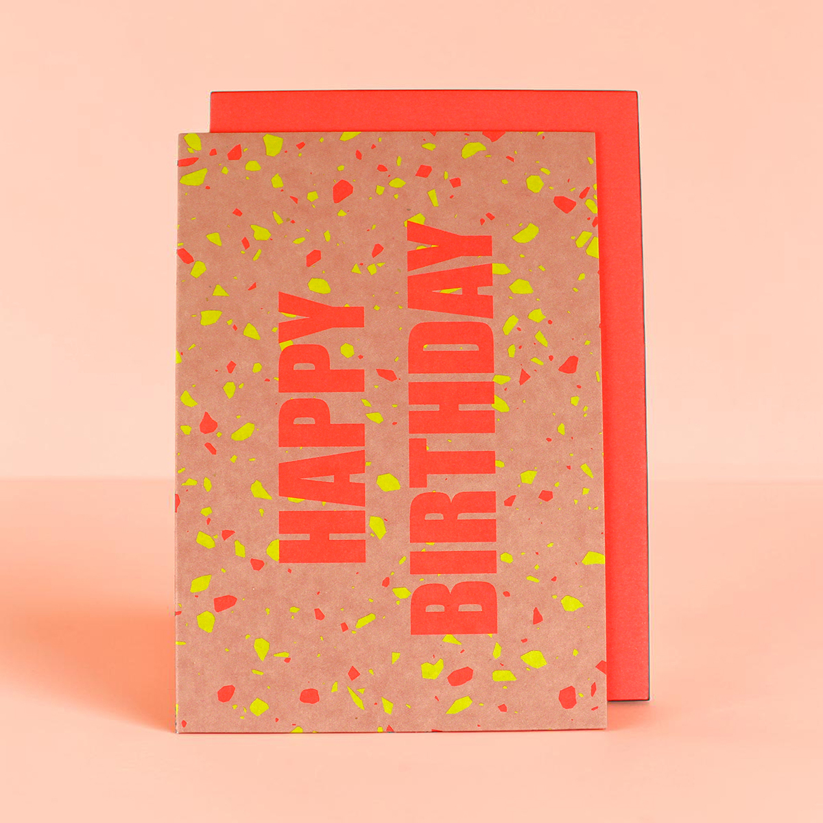 Brown kraft gift box with bold coral 'HAPPY BIRTHDAY' text and neon confetti on a peach background.