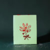 4178geschenktaschesmistelzweig02 Avayves Feine Papeterie Und Geschenke Für Babys Und Kids Light green gift box with a red ribbon bow on a dark surface, with white specks scattered around the base area.