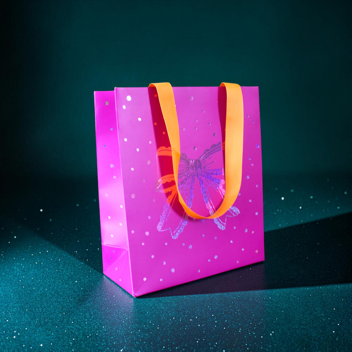 4180geschenktaschemschleife Avayves Feine Papeterie Und Geschenke Für Babys Und Kids Pink gift bag with orange handles on a dark teal speckled background, festive and ready for gift-giving.