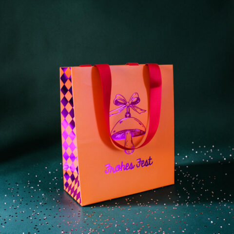 Orange gift bag with pink handles and a purple bow, on a teal background with scattered confetti.