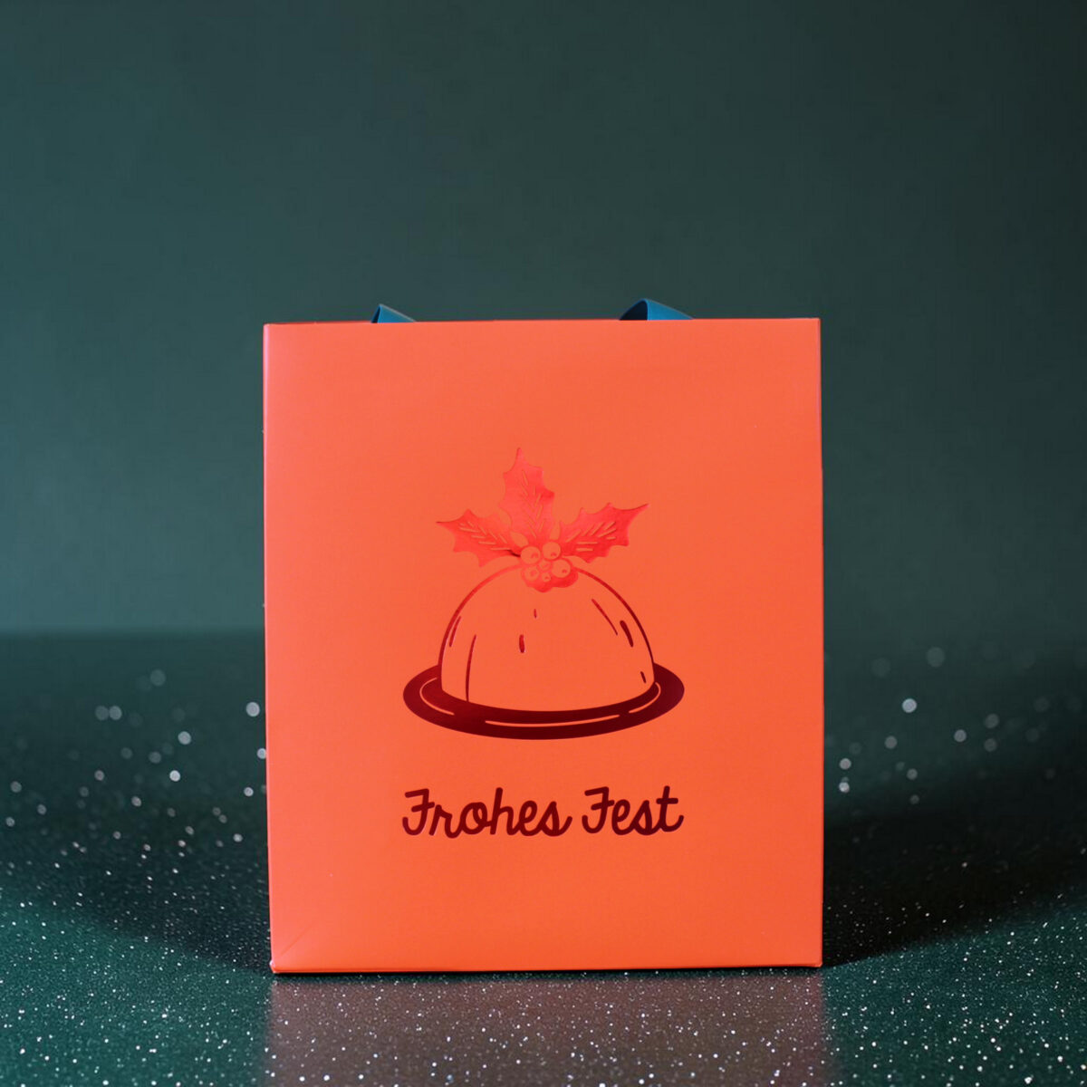 4182geschenktaschemchristmaspudding02 Avayves Feine Papeterie Und Geschenke Für Babys Und Kids Orange gift box with a blue ribbon peeking out, holly illustration, and the text 'Frohes Fest' on a dark snowy backdrop