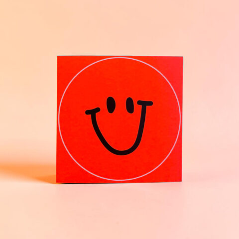 Red square box featuring a bold black smiley face inside a white circular outline on a bright red background.