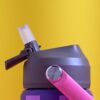 Close-up of a gray sports bottle with a spout on a pink and purple water bottle, against a bright yellow background.
