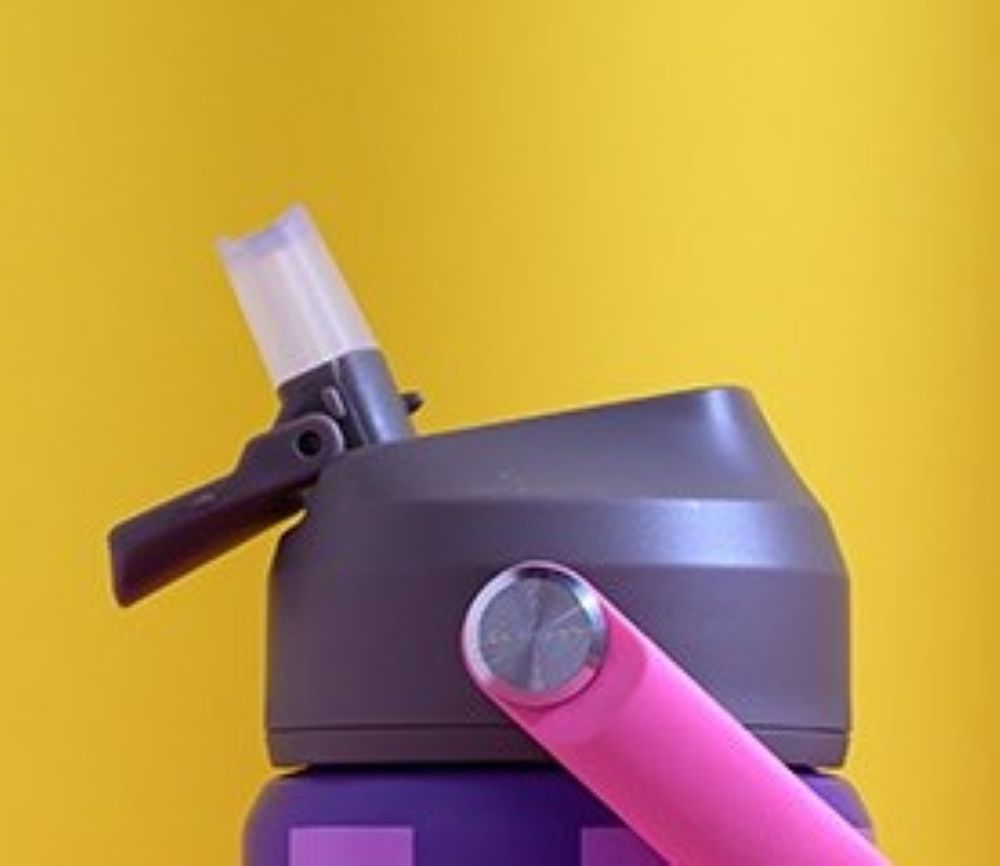 Close-up of a gray sports bottle with a spout on a pink and purple water bottle, against a bright yellow background.