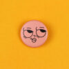 Pink round button with a sleepy, kissy-face emoji on a bright yellow background, centered in the image