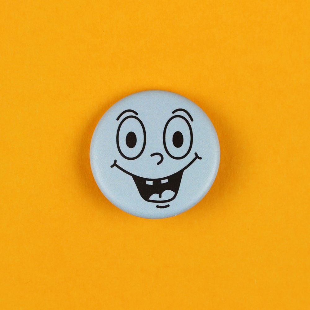 6293buttongesichthellblau Avayves Feine Papeterie Und Geschenke Für Babys Und Kids Blue circular button with a cartoon smiling face on an orange background.
