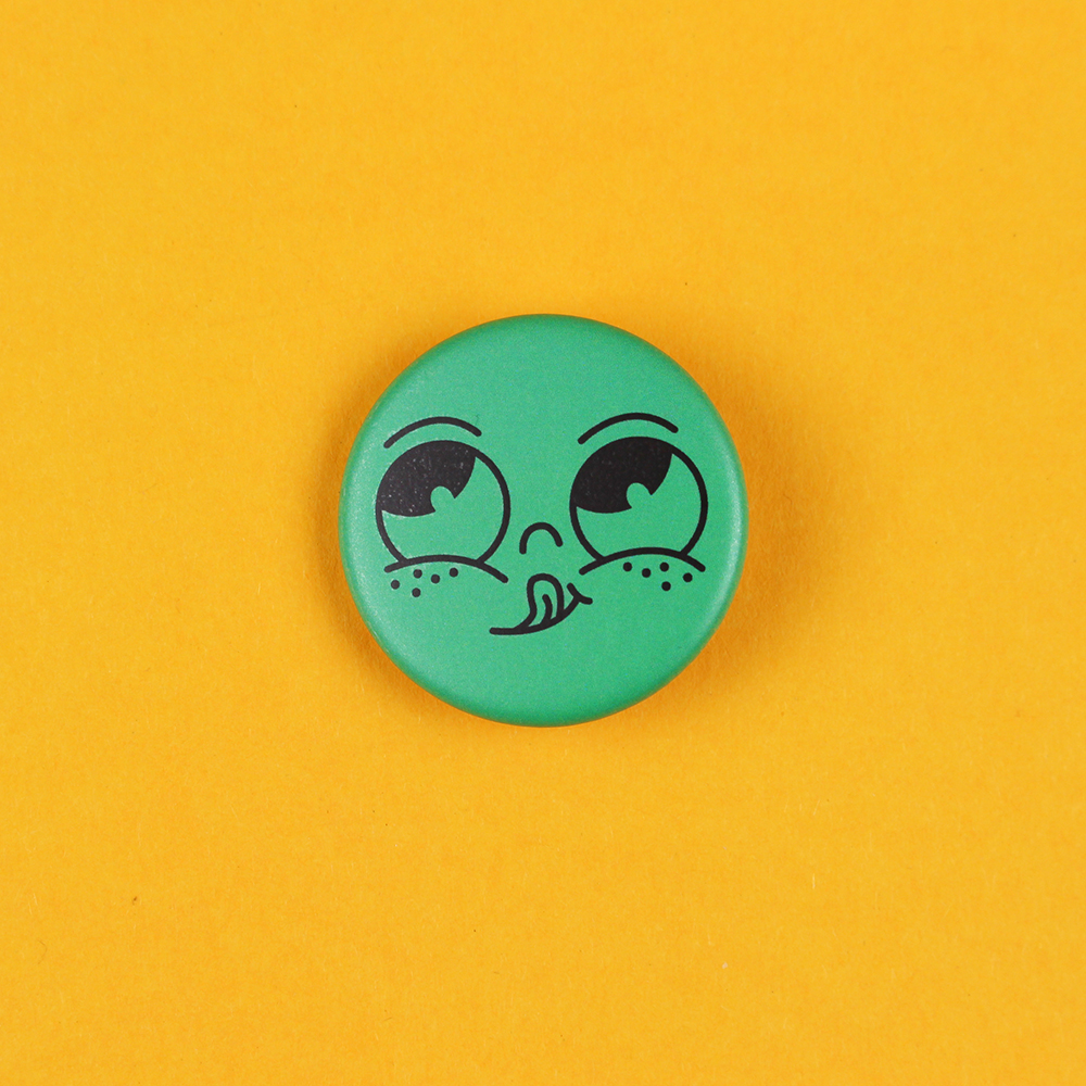 Green circular button with a cartoon face sticking out its tongue on a bright yellow background