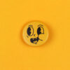 Close-up of a yellow round emoji button with a goofy, tongue-out facial expression on a yellow background.