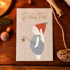 German holiday card on a wooden desk with gold 'Frohes Fest' text and a cartoon snowman holding a star wand under falling snow
