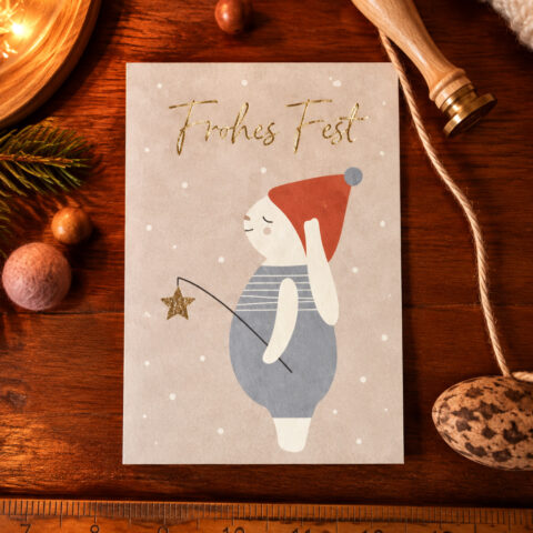 German holiday card on a wooden desk with gold 'Frohes Fest' text and a cartoon snowman holding a star wand under falling snow