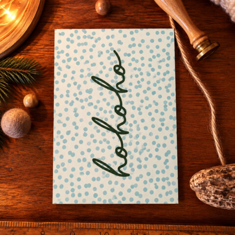 Greeting card with a spiral green Christmas tree on a blue polka-dot background, placed on a wooden table with festive decor nearby.