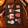 Christmas-themed illustrated card featuring a red mitten, drum, tree, gift box, house, snowman, stocking and ice skate on a dark background.