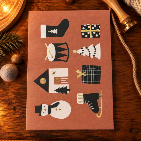 Festive collage on a brown card showing cutout shapes: sock, present, drum, stacked tree, house, plaid gift bag, snowman, Christmas tree slices, and ice skate.
