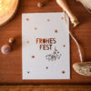 1280pkfrohesfestmistelzweig Avayves Feine Papeterie Und Geschenke Für Babys Und Kids Overhead view of a white holiday card with copper stars on a wooden surface, with a string, a ruler at the bottom, and warm light nearby.