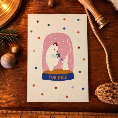 Card featuring a white bear and a bunny inside a pink snow globe with 'FÜR DICH' on a blue pedestal, festive confetti around.