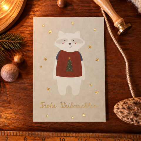 Beige Christmas card with a white bear in a red sweater and a Christmas tree, surrounded by gold stars on a wooden surface.
