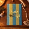 1370pkfrohefesttage Avayves Feine Papeterie Und Geschenke Für Babys Und Kids Holiday card on a wooden table with blue and gold stripes and gold script reading 'Frohe Festtage' surrounded by rustic décor.