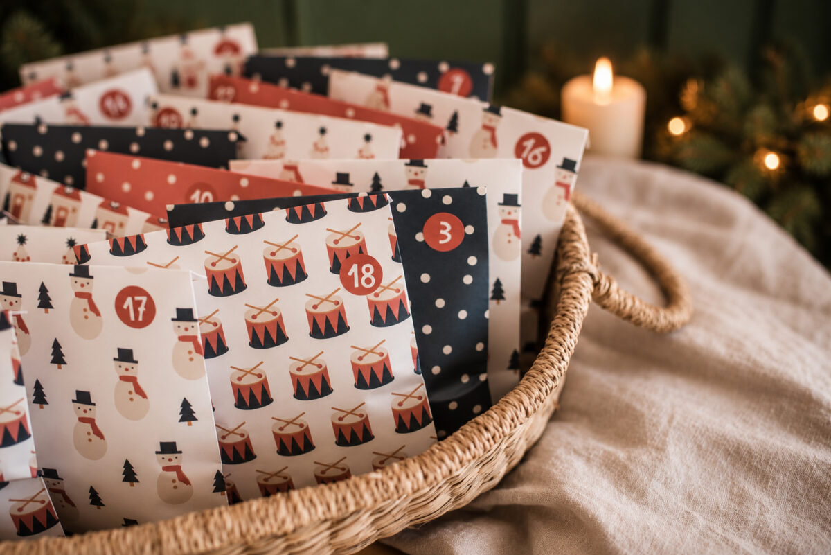 4138adventcalendarhaeuser03 Avayves Feine Papeterie Und Geschenke Für Babys Und Kids Decorative Advent calendar bags arranged in a woven basket with festive patterns and red numbers.
