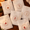 White gift envelopes on a wood table, each with a brown circular stamp of Christmas icons (tree, snowman, stocking, house).
