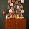 Mid-century wooden sideboard against a dark green wall, topped with a copper-striped paper advent calendar arranged as houses with numbers.