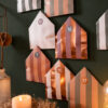 Advent calendar with metallic striped paper house shapes on a dark green wall, numbers like 3, 13, 15 visible.