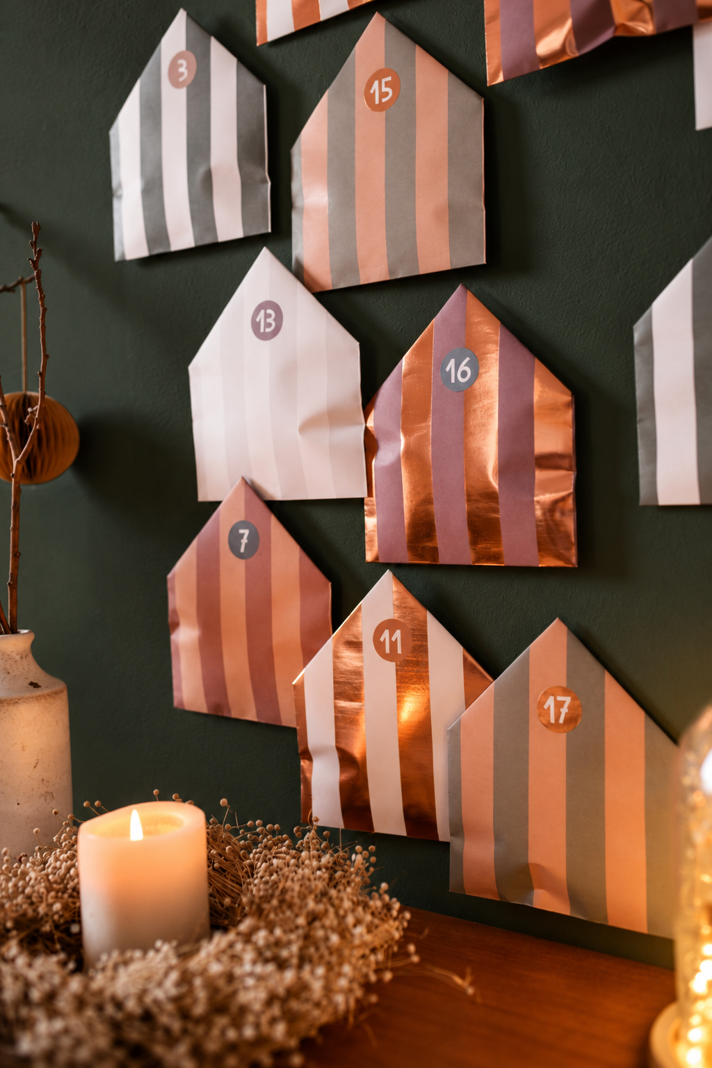 Advent calendar with metallic striped paper house shapes on a dark green wall, numbers like 3, 13, 15 visible.